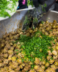 Olives being mixed in a bowl, covered in pomegranate molasses, walnuts and parsley