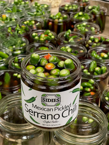 An open jar of Mexican pickled serrano chilies sitting on top of other open jars of pickled chilies